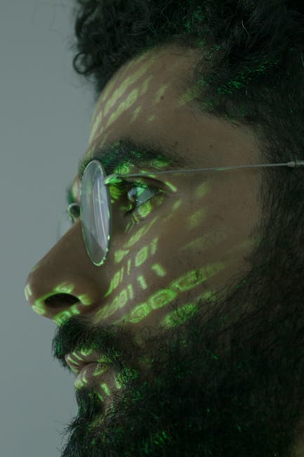 A close-up view of a person's hands using a laptop on a dark, smooth surface. The laptop screen displays a code editor with lines of colorful code in various shades of green, blue, and white on a dark